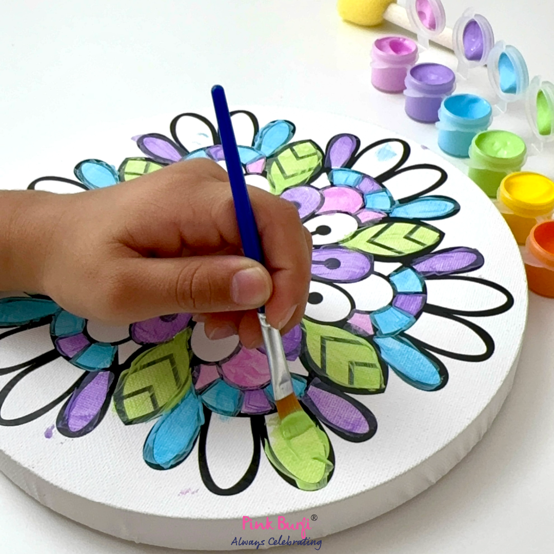 Close up of child painting a colorful mandala on a white board with various colors and tools around from the Pink Burfi Resist Art Canvas Rangoli Box.